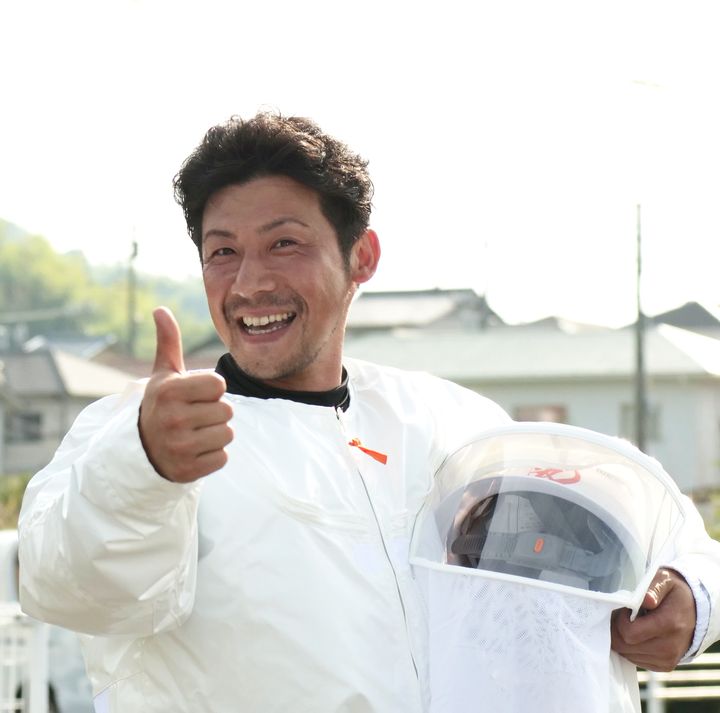 防護服を着て笑顔で親指を立てるBee-zone担当責任者の高林佑三